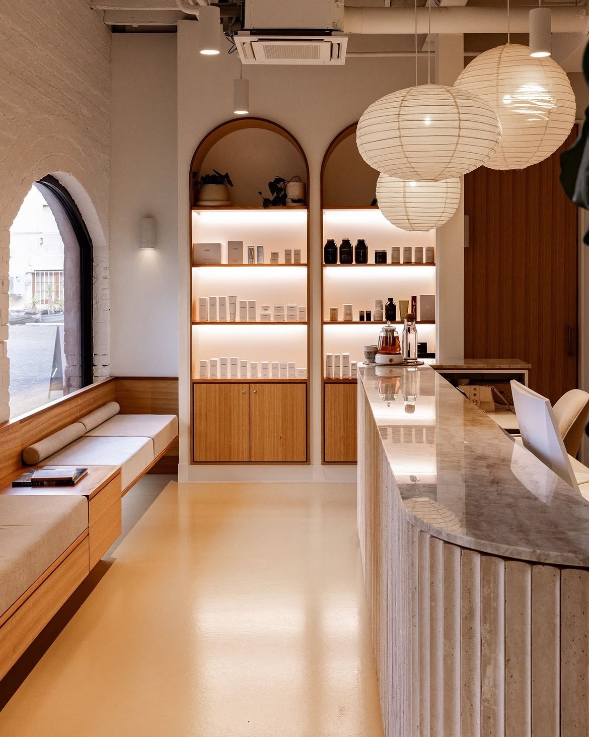 A welcoming, premium Hobart cosmetic clinic interior with warm timber shelving, soft paper lanterns and a marble reception counter